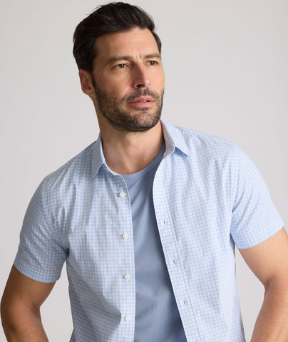 Model is wearing UNTUCKit Dunbar short sleeve shirt in blue and white Dimond print. 